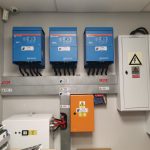 Three inverters mounted alongside an electrical enclosure in a plant room