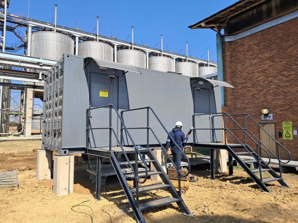 Site technician in hard hat beside a containerised plant room under installation