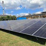 Ground-mounted solar PV array with industrial plant in the background
